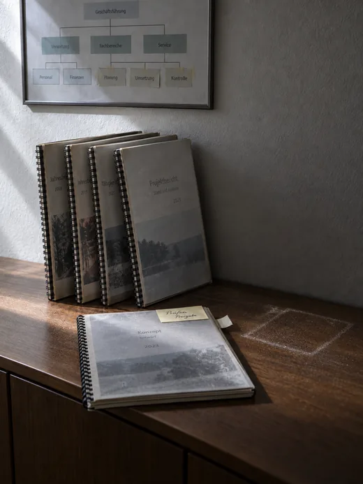 Vier spiralgebundene Beratungsberichte auf dem Sideboard im Flur, keiner je weit aufgeschlagen
