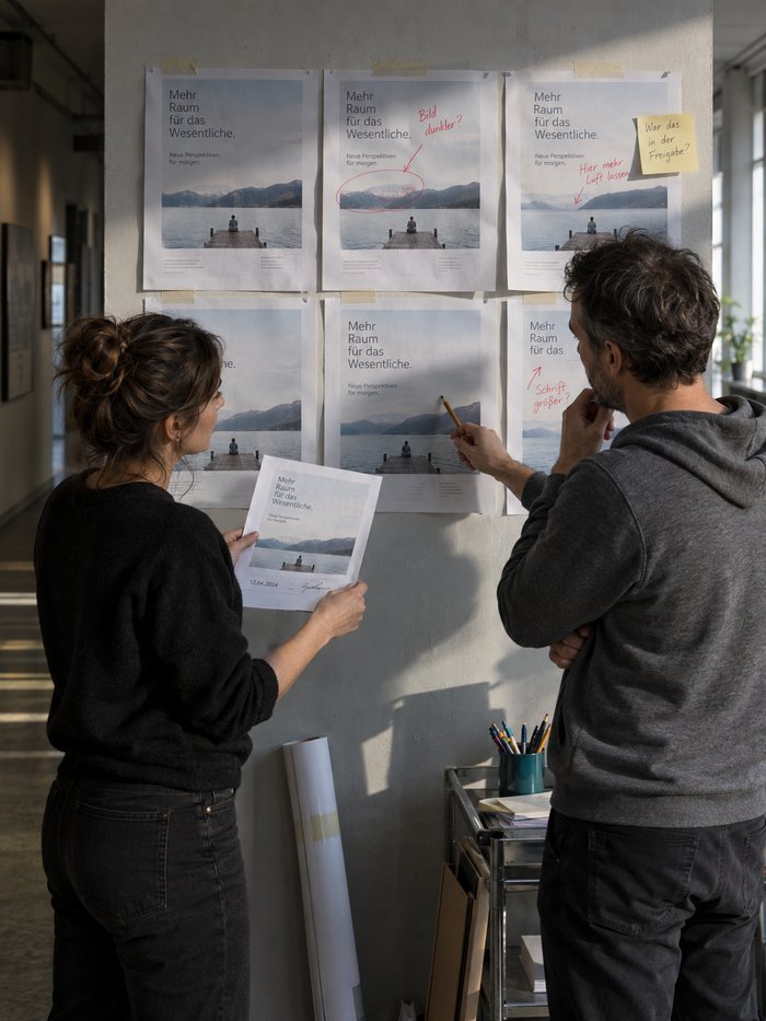 Projektmanagerin hält den Freigabeausdruck gegen die Layoutstände an der Wand des Agenturflurs