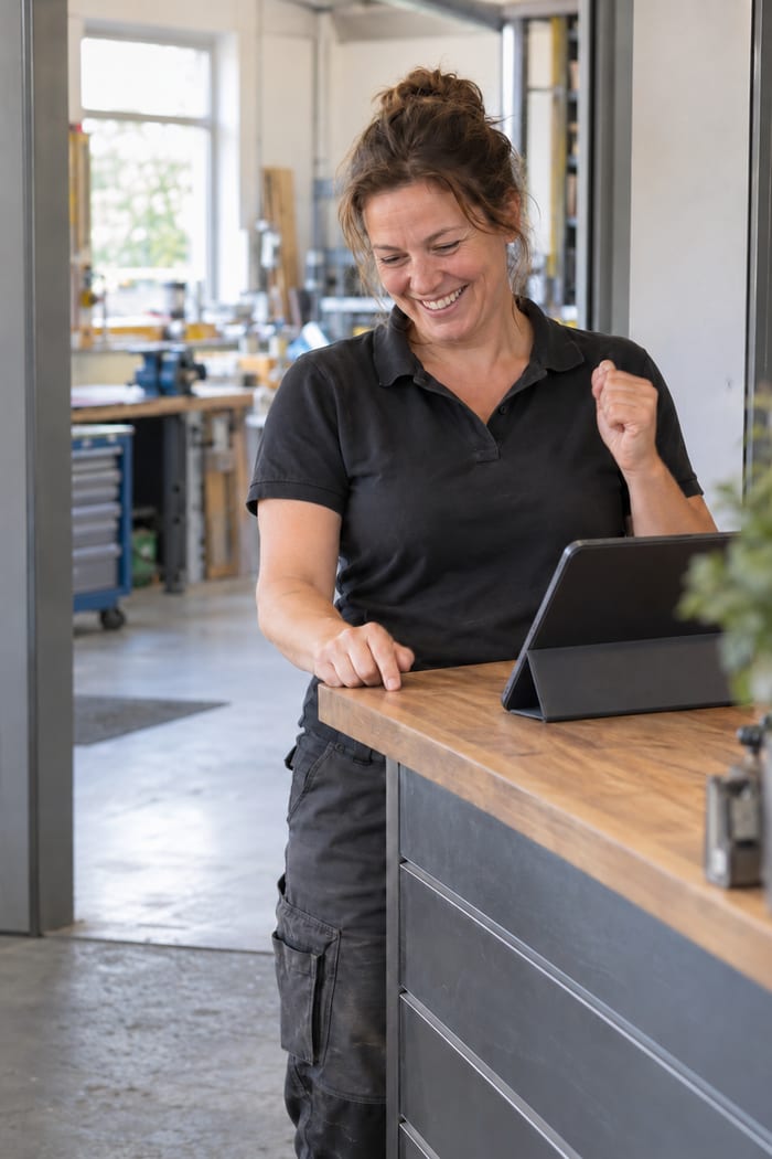 Handwerksmeisterin an der Kundentheke freut sich über den fertig angenommenen Auftrag im digitalen Auftragsblock auf dem Tablet