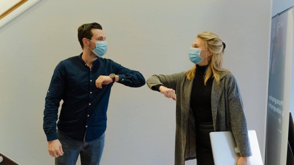 Zwei Mitarbeitende in Masken grüßen sich via Ellenbogencheck