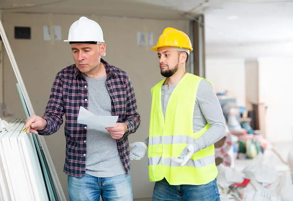 Verwirrter Bauarbeiter, der neben seinem Kollegen steht, während Materialien geprüft werden