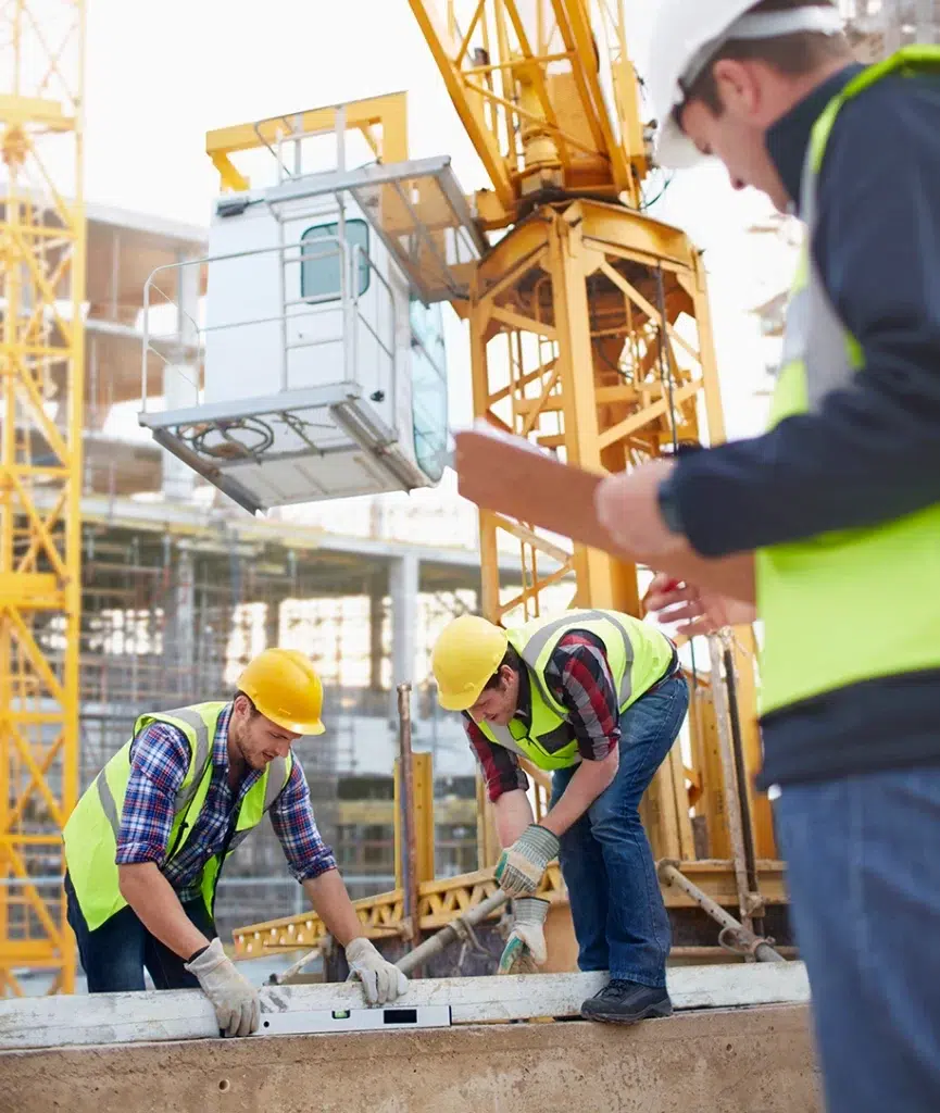 Bauarbeiter arbeiten mit einer Wasserwage auf einer Baustelle, ein weiterer Arbeiter führt Notizen durch