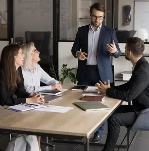 Geschäftsmann steht und spricht zu einer Gruppe von Fachleuten, die am Konferenztisch sitzen