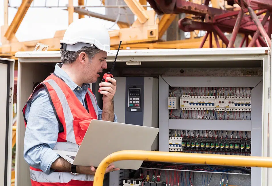 Elektriker mit Laptop-Computer führt die Wartung des elektrischen Systems auf der Baustelle durch
