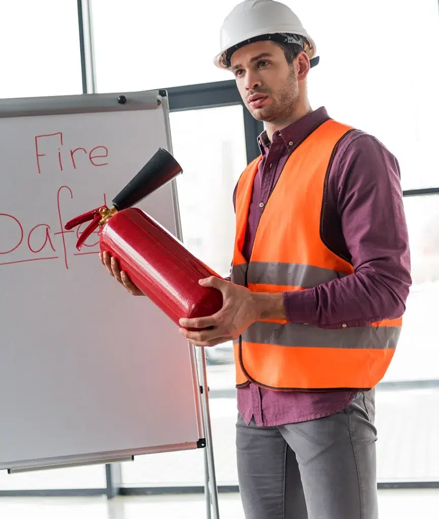 Feuerwehrmann mit rotem Feuerlöscher in der Hand und neben einer weißen Tafel mit Brandschutzaufschrift stehend
