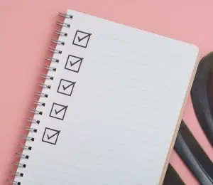 Ein leeres Notizbuch mit einer Checkliste, die ausgefüllt und deren letztes Kästchen angekreuzt wird