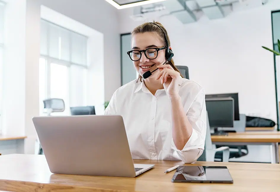 Eine Geschäftsfrau sitzt in einem Büro, führt ein Telefonat und macht sich am Laptop Notizen