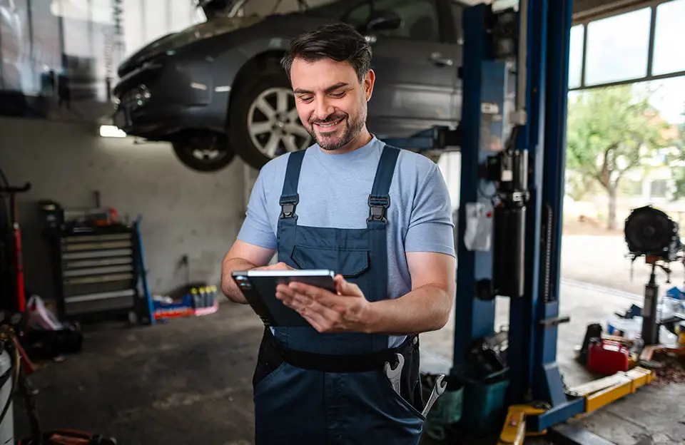 Ein Automechaniker mit Tablet steht vor einer Hebebühne mit Fahrzeug