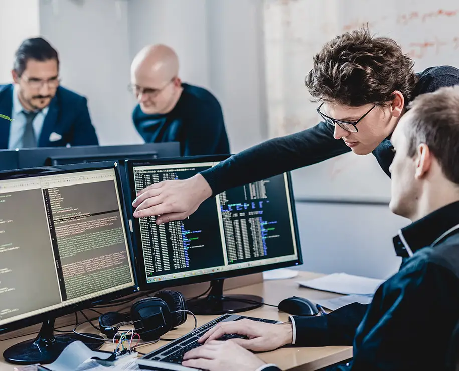 Zwei Entwickler in einem Büro beraten sich über zwei Bildschirmen