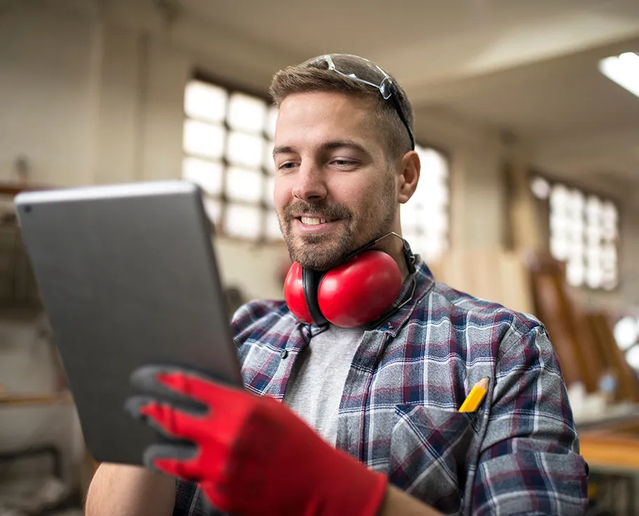 Ein Handwerker mit Schallschutz und Schutzhandschuhen mit einem Tablet